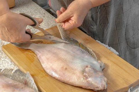 Chef uses scissors to cut out a fin from a fresh flounder Stock Photos