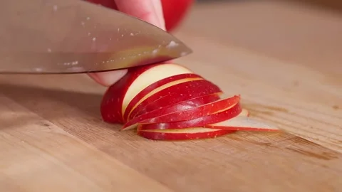The chef uses a sharp knife to cut red apples into thin slices on a wooden board Stock Footage 267010763