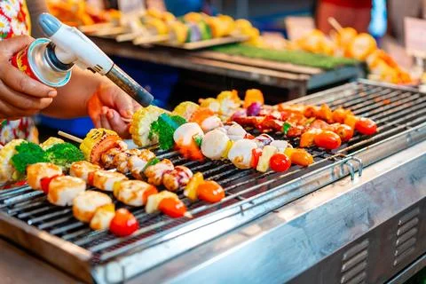 Chef using flame torch to burn scallop BBQ sticks at street food night market 库存照片