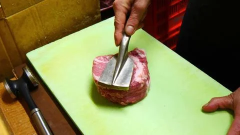 Chef using a metal tenderizer tool on raw meat on a cutting board Stock Photos