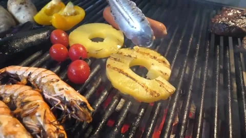 Chef using metal tongs to flip grilled pineapple slices and shrimp on a hot barb 库存影片 338213388