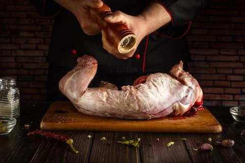 A chef is using a pepper grinder to season a large piece of raw meat on a woo Stock Photos