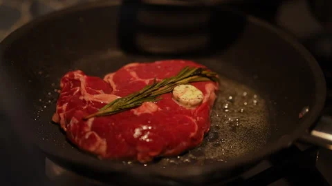 Chef using spatula to turn juicy rib eye steak seasoned with sprig of rosemary Stock Footage 290073096