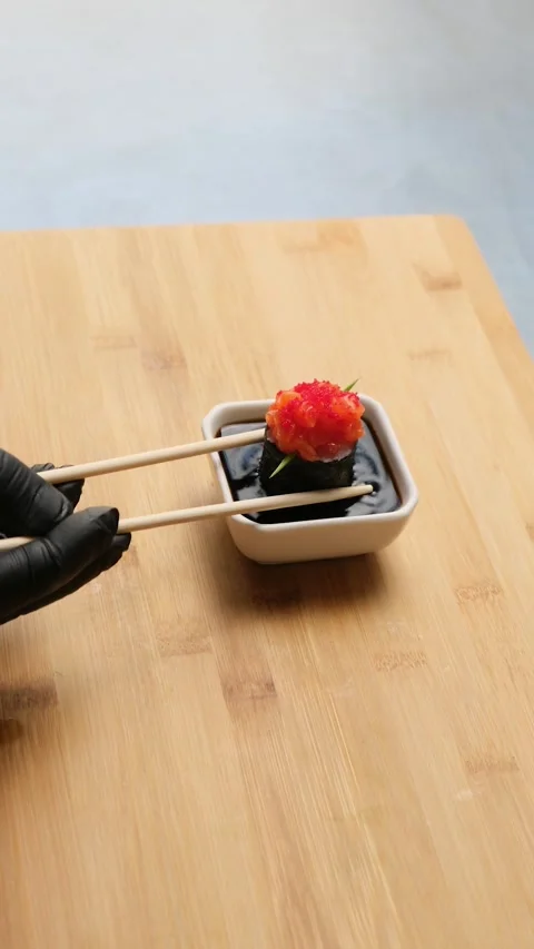 The chef using sushi chopsticks, takes the roll and dips it in soy sauce. Stock Footage 262581996