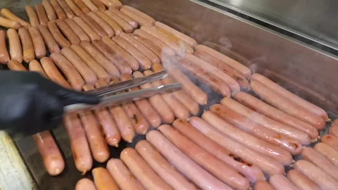 Chef using tongs to align and grill sausages on a professional hot flat griddle Stock Footage 324710862