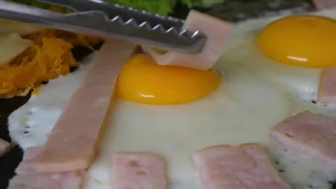 Chef Using Tongs to Arrange Sliced Ham on Fried Eggs on a Griddle Stock Footage 345692721