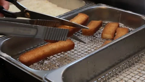 Chef using tongs to handle crispy golden brown fried fish fingers in a professio Stock Footage 333569655