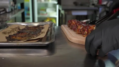 The chef using tongs lays out delicious juicy pork ribs on a wooden plate. Stock Footage 287583159