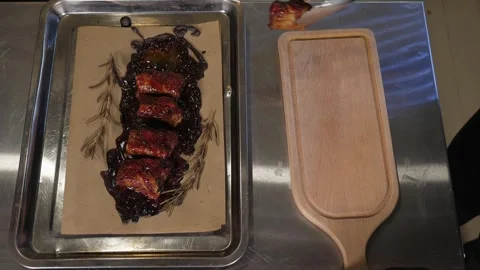 Chef using tongs lays out juicy pork ribs on a wooden plate in the restaurant. Stock Footage 345132928