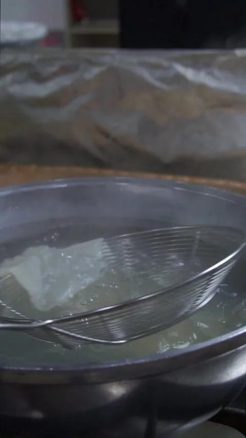 Chef using a wire skimmer to place the first boiled dough sheet into a carved wo Stock Footage 342627886