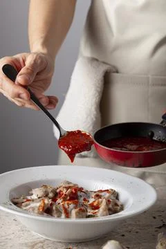 A  chef wearing apron is adding fresh tomato sauce to homemade Turkish manti Stock Photos