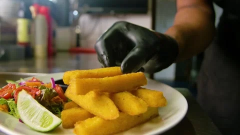 Chef wearing black rubber gloves places polenta fries on a stack, white Stock Footage 255010503