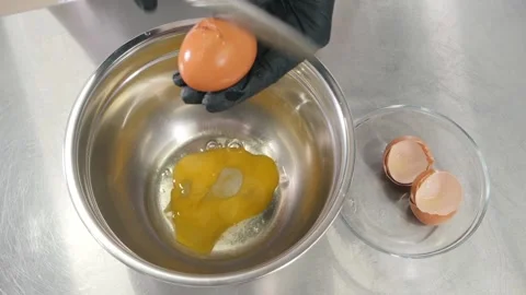 Chef wearing gloves breaks egg with knife over metal bowl Stock Footage 137932165