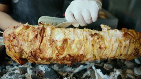 Chef wearing gloves cutting roasted meat from a gyros spit rotating over hot Stock Footage 343223718