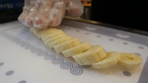 Chef wearing plastic hygiene gloves lining up sliced banana rounds on a patterne Stock Footage 345692791