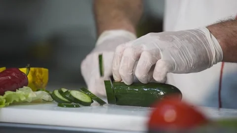 Chef in white gloves skillfully slicing cucumber on a cutting board, showcasing Видео 330595425