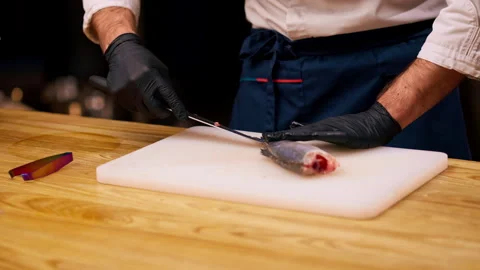 A chef in a white jacket in a professional kitchen cuts fish with knife before Stock Footage 273628951