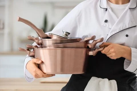 Chef in white uniform holding a stack of copper cooking pots and pans with li Stock Photos