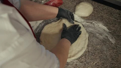 Chef in white uniform uses hands to shape pizza dough on a granite countertop, Vídeo Stock 332736603
