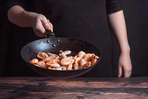Chef at work. Hand holds a hot pan with fried shrimp. Stock Photos