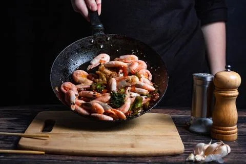 Chef at work. Hand holds a hot pan with fried shrimp and vegetables in sweet  Stock Photos