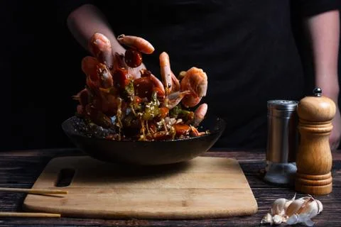 Chef at work. Hand holds a hot pan with fried shrimp and vegetables in sweet  Stock Photos