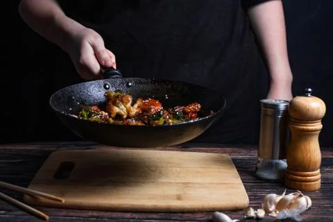 Chef at work. Hand holds a hot pan with fried vegetables, broccoli, cauliflow Stock Photos