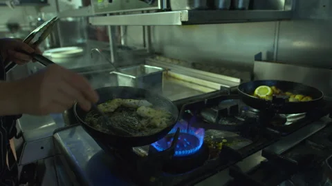 Chef working in restaurant kitchen hot flame stove basting fish with butter 库存影片 330977224