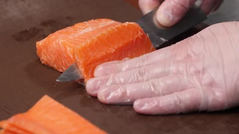 The chef's gloved hand cuts salmon meat into thin pieces with a knife. Video stock 289080730