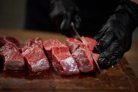 Chef's gloved hands cutting raw beef cubes Stock Photos