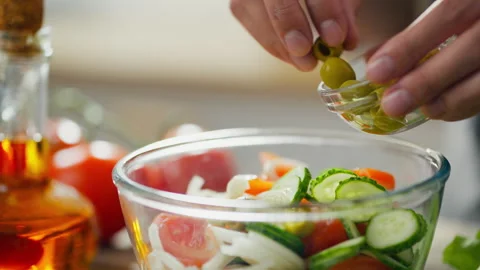 Chef's hand is adding olives to glass bowl with the salad. Preparing healthy 動画素材 246743969