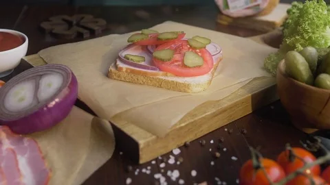 Chef's hand adds sliced bacon to the sandwich with tomatoes and pickles, cooking Stock Footage 112643467