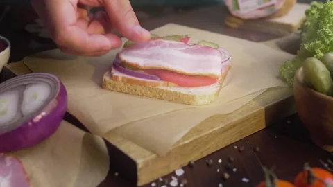 Chefs hand adds sliced bacon to the sandwich with tomatoes and pickles Stock Footage 143780384