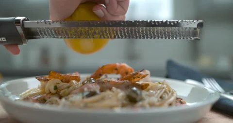 A chef's hand grates a lemon over a white plate of shrimp and olive linguini in Stock Footage 199459728