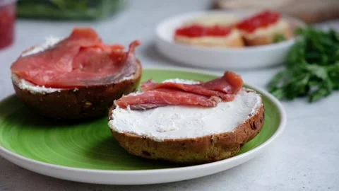 A chef's hand places slices of red salmon onto a sesame dark bread with cream Stock Footage 101480183
