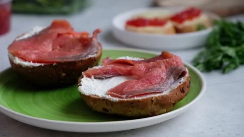 A chef's hand places slices of red salmon onto a sesame dark bread with cream Vídeos de archivo 101481086