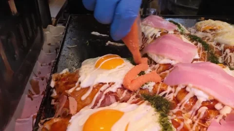 Chef's Hand Plating Slices of Bacon on Japanese Okonomiyaki Savory Street Food P Stock-Footage 347688958