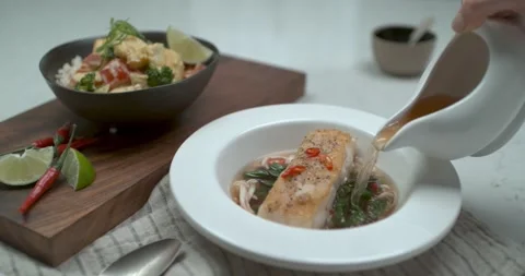 A chef's hand pours fish broth into a porcelain bowl from a white jug over a tab Stock Footage 199455784
