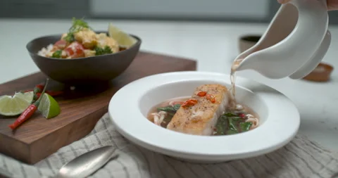 A chef's hand pours fish broth into a porcelain bowl from a white jug over a tab Stock Footage 199457107
