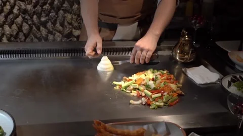 Chef's hand setting fire to a pyramid of chopped onions on a teppanyaki grill Stock Footage 279129015