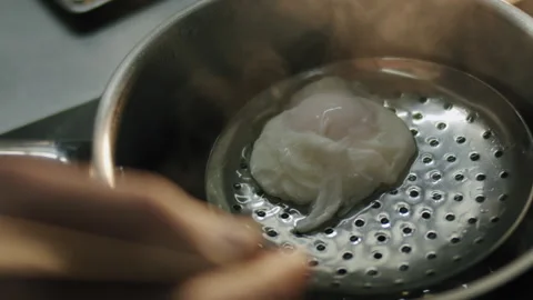 The chef's hand with a slotted spoon takes out a poached egg from boiling water 스톡 동영상 150762778