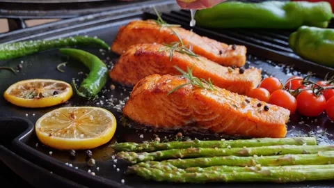 Chef's hand is squeezing a fresh lemon over grilling fillet salmon. Slow motion. Stock Footage 246770414