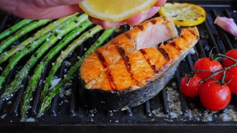 Chef's Hand Is Squeezing A Fresh Lemon Over Grilling Steak Salmon. Slow Motion. Video stock 252450908