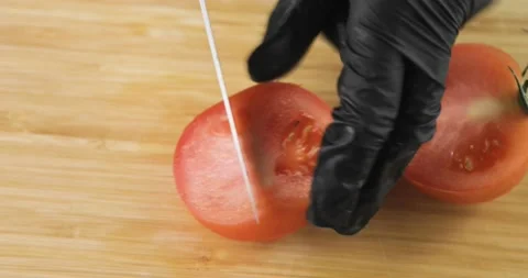 Chef's hands in black gloves cutting fresh tomato into pieces on wooden board. Stock Footage 147432698