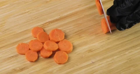Chef's hands in black gloves cutting fresh carrot into slices on wooden board. Stock Footage 147433762