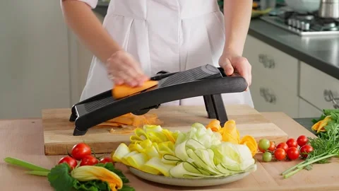 Chef's hands dangerously grate young carrots with slices on a mandalin grater Stock Footage 264141604
