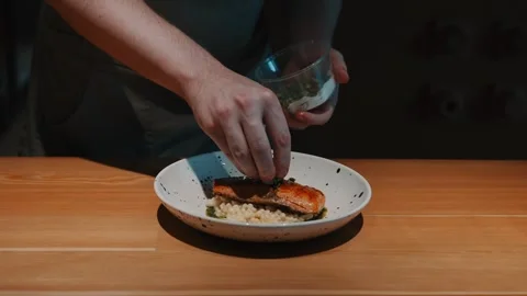 Chefs hands decorating grilled salmon steak garnished with ptitim and greens Stock Footage 318072433