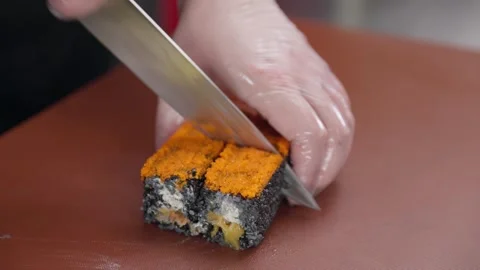 The chef's hands in gloves cut sushi with a knife sprinkled with fish roe. Stock-Footage 281558025