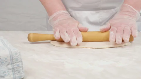 The chef's hands in gloves roll out the dough with a wooden dough roller. Stock Footage 149166677