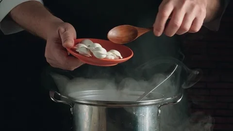 Chef's hands gracefully pour dumplings from an orange plate into a steaming pot, Stock Footage 334891570